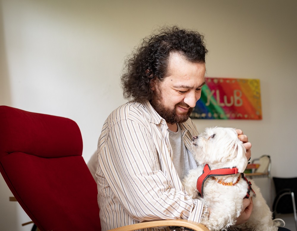 Eine leistungsberechtigte Person sitzen im Sessel mit der Therapiehündin auf dem Schoß. Eine leistungsberechtigte Person sitzen im Sessel mit der Therapiehündin auf dem Schoß.