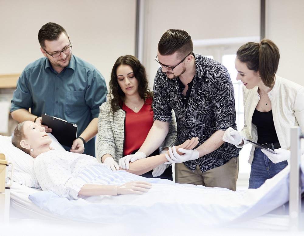 Auszubildende stehen an einem Krankenbett und üben an einer Puppe. Auszubildende stehen an einem Krankenbett und üben an einer Puppe.